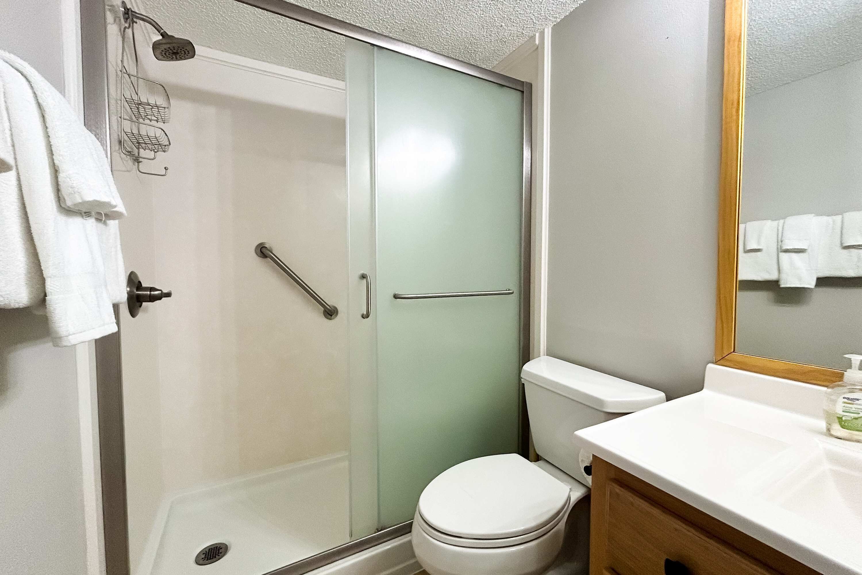 Un bagno con cabina doccia in vetro, un water, un lavandino con specchio e un portasciugamani.