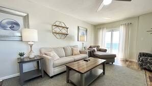 A living room with a sofa, coffee table, side tables, and a ceiling fan. - Oceanfront condo with pool, grilling area, alfresco dining, internet, W/D, & AC (Gulf Shores)