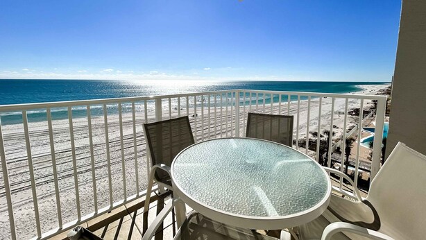 A balcony with a glass table and chairs, overlooking a beach and a pool area. - Oceanfront condo with pool, grilling area, alfresco dining, internet, W/D, & AC (Gulf Shores)