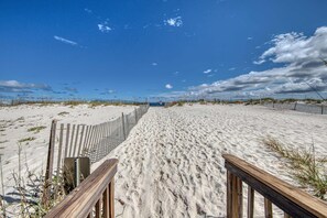 Ein sandiger Strand mit einer Holzstege, der zu einer Gebäudes in der Ferne führt.