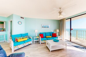Ein Wohnzimmer mit einer Couch, einem Couchtisch und Sesseln, einem Deckenventilator und Blick auf den Ozean durch eine Schiebetür.