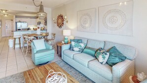 A living room with a sofa, coffee table, and a dining area with chairs and a table. - Gulf view condo with resort amenities, scenic balcony, open layout, W&D, & AC (Gulf Shores)