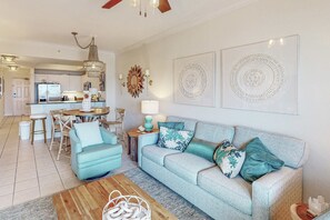 A living room with a sofa, coffee table, and a dining area with chairs and a table. - Gulf view condo with resort amenities, scenic balcony, open layout, W&D, & AC (Gulf Shores)