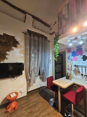 A modern interior with a flat-screen TV mounted on the wall, grey curtains, a wooden floor, red chairs, and a small orange stool. - Cozy apartment in a typical Lombard courtyard (Vanzago)
