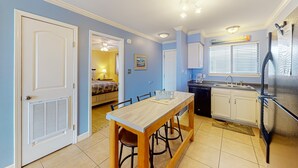 Ett kompakt kök med ett matbord, stolar, ett kylskåp och ett fönster med persienner.