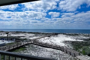 A coastal view with a wooden boardwalk leading to the beach, a clear sky, and the ocean in the distance. - Bright oceanfront condo with pool, hot tub, sauna, tennis & central AC (Gulf Shores)