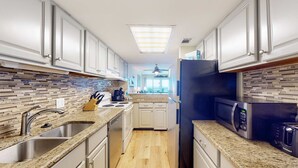 A modern kitchen with granite countertops, stainless steel appliances, and a tiled backsplash. - Inviting condo with ocean view, on-site pool, cozy balcony, washer/dryer & AC (Gulf Shores)