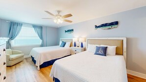 A hotel room with two beds, a ceiling fan, a window with curtains, a nightstand, and a chair. - Inviting condo with ocean view, on-site pool, cozy balcony, washer/dryer & AC (Gulf Shores)