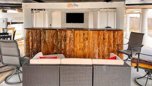 Zona de bar amb paret decorativa de fusta, televisió de pantalla plana i un conjunt de seients amb cadires i un sofà.