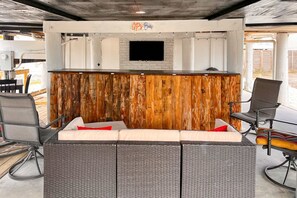A bar area with a wooden accent wall, a flat-screen TV, and a seating arrangement with chairs and a sofa. - Dog-friendly beach stay with a balcony, grill, outdoor bar, swing, W&D, & AC (Gulf Shores)