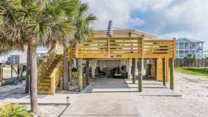 Una construcció de fusta al costat de la platja, amb una escala, zona d'estar coberta i vista a l'oceà.