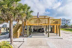 Une structure en bois située au bord de la plage, dotée d’un escalier, d’un espace de repos couvert et offrant une vue sur l’océan.
