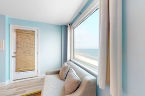 Ein Zimmer mit Meerblick, einer Couch, einer Tür mit Bambusrollvorhang und einem Fenster mit Vorhängen.