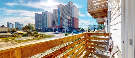 A balcony with wooden railings overlooking a street with tall buildings and a clear sky.