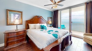 Habitación de hotel con cama, mesita de noche, cómoda, ventilador de techo y balcón con vistas.