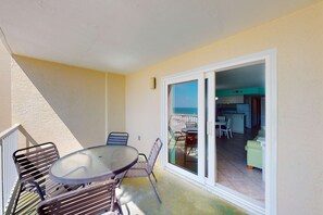 A balcony with a table and chairs, a sliding glass door leading to an interior space with a dining area and a sofa. - 2nd-floor Gulf-front condo with amazing beach views, balcony, outdoor pool & W/D (Gulf Shores)