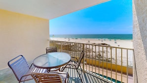 Een balkon met een tafel en stoelen, met uitzicht op een strand en een heldere lucht.
