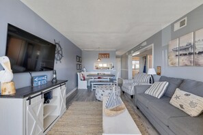 A modern living room with a grey sofa, striped armchairs, and a flat-screen TV mounted on the wall. A wooden sign reads "ONE WAY TO THE BEACH". - Ganti's Shanty - Ocean Views, Walkable to CB Boardwalk (Carolina Beach)