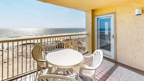 Un balcón con vista a la playa, una mesa con sillas y una puerta.