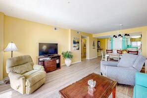 A living room with a sofa, a television, a lamp, and a coffee table. - Fourth-floor Gulf-front getaway with balcony, views, central AC, & outdoor pool (Gulf Shores)