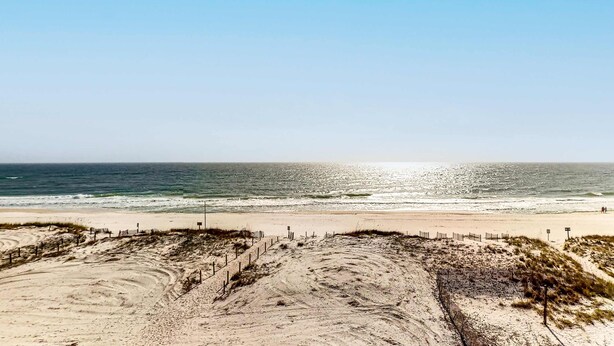 Una playa con un sendero arenoso que conduce al océano, una valla y un cielo despejado.