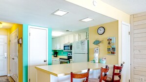 Cocina con armarios blancos, microondas y refrigerador. Hay un reloj en la pared y una pequeña decoración con forma de pez.