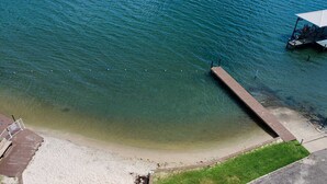 Une plage avec une jetée en bois qui s’avance dans l’eau, une zone herbeuse et un bâtiment doté d’un toit.