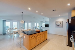 A spacious kitchen with a large island, wooden cabinets, and a dining area with a table and chairs. - Lovely beachfront home with balcony, central AC, & washer,dryer (Gulf Shores)