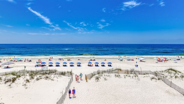 Ein Strand mit weißem Sand, einem hölzernen Zaun und blauem, wolkenlosem Himmel.