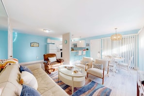 A living room with a sofa, armchairs, a coffee table, and a dining area with a table and chairs. - Upgraded beachfront condo with a pool, beach access & washer,dryer (Gulf Shores)