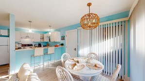 Een moderne keuken met witte kasten, een eettafel met stoelen en een hangende lamp.