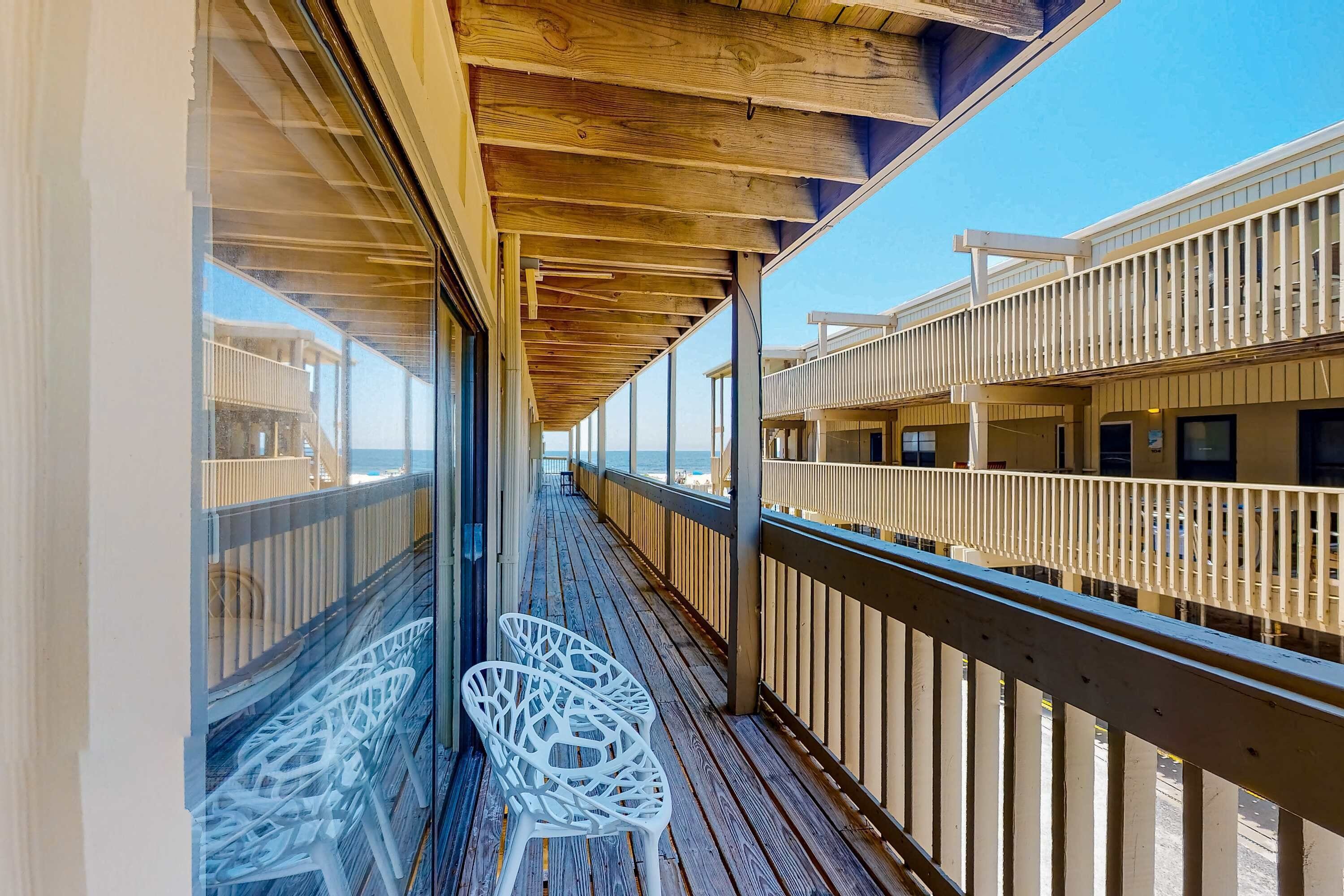 Une terrasse en bois avec des rampes en verre, des chaises blanches et une vue sur l’océan.