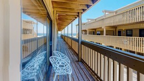 Eine Holzterrasse mit Glasgeländern, weißen Stühlen und Blick auf den Ozean.