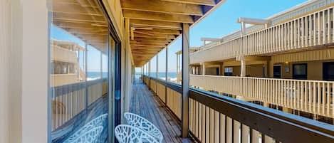 Une terrasse en bois avec des rampes en verre, des chaises blanches et une vue sur l’océan.