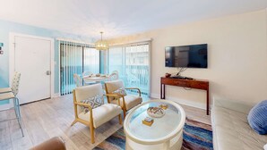 Ein Wohnzimmer mit Glastisch, zwei Sesseln, einer Couch, einem Fernseher und einem Balkon mit Blick.