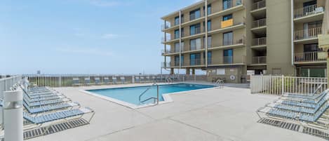 A pool area with lounge chairs and a building with multiple balconies.