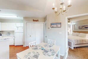 A compact kitchen with white cabinets, a refrigerator, and a dining table with floral placemats.