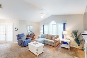 A living room with a sectional sofa, a blue armchair, a white coffee table, a small white side table, and a ceiling fan.