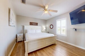 Une chambre à coucher comprenant un lit, un ventilateur de plafond, une télévision, une table de chevet, une horloge murale et une fenêtre.