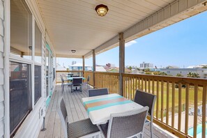 Une terrasse extérieure couverte, avec une table et des chaises, offrant une vue sur la ville et donnant sur une piscine à l’arrière-plan.