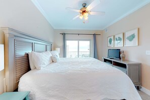 Ein Schlafzimmer mit einem großen Bett, einem Deckenventilator, einem Fernseher und einem Balkon mit Vorhängen.