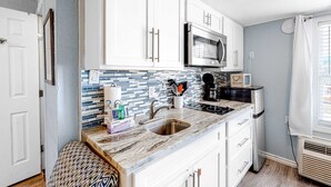 A compact kitchen with white cabinets, a stainless steel microwave, a tiled backsplash, and a built-in sink.