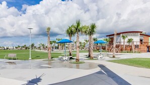 A modern building with a curved roof, surrounded by palm trees and blue umbrellas.