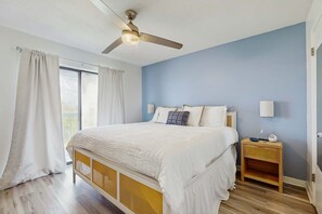 Ein Schlafzimmer mit Bett, Nachttisch, Deckenventilator und einem Fenster mit Vorhängen.