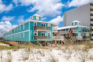 A beachfront hotel with multiple stories, wooden balconies, and a sandy beach in the foreground. - Beachside home steps from the water with pool access & central AC (Gulf Shores)