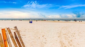 Una playa arenosa con una cerca de madera, una torre de salvavidas y gente a lo lejos.
