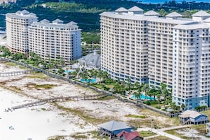 Ein Hochhaus-Hotel mit mehreren Balkonen, einem Zugangsweg zum Strand und einem Poolbereich.