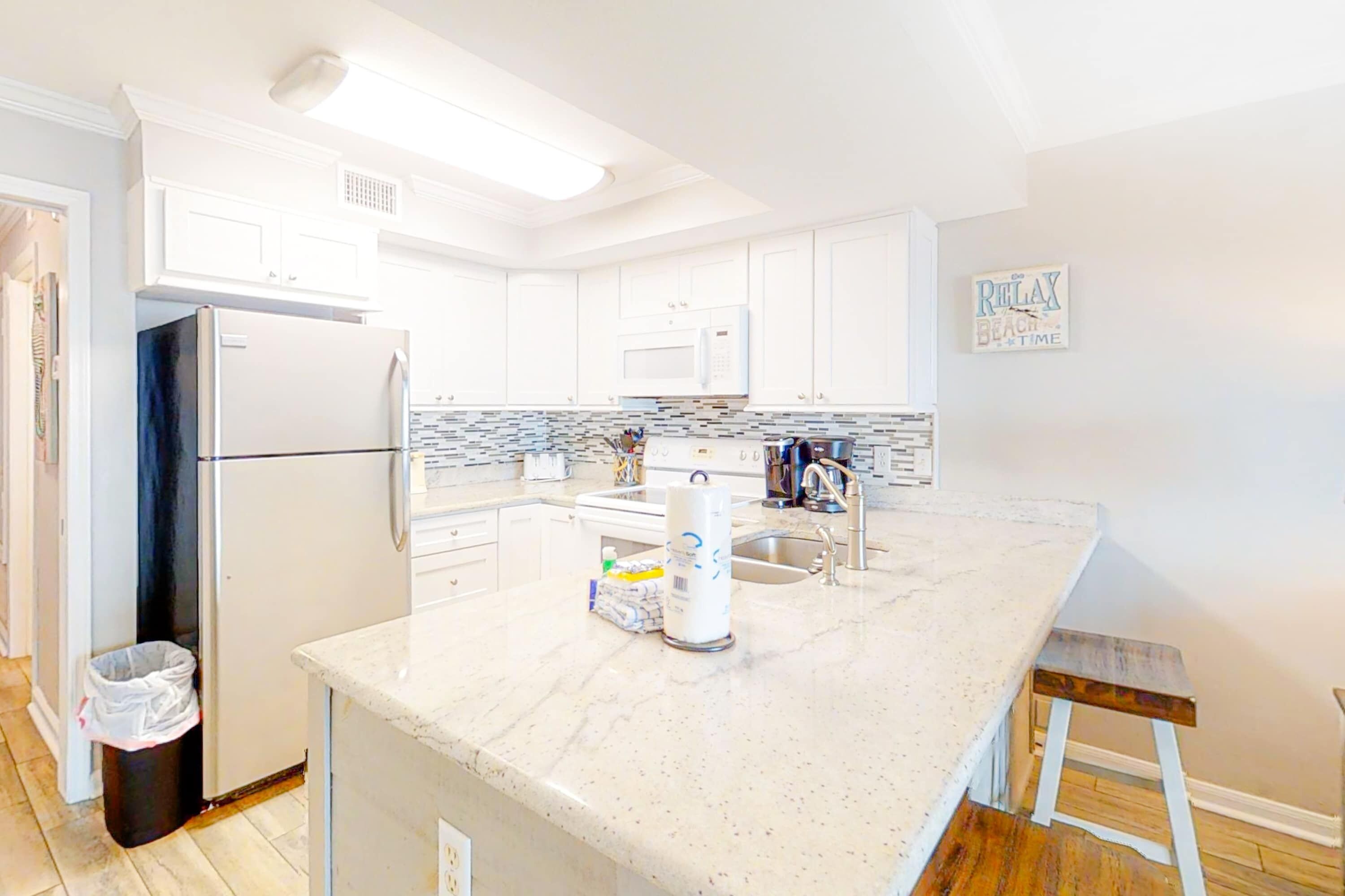 A modern kitchen with white cabinets, a marble countertop, a refrigerator, a microwave, and a sink.