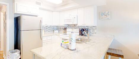 A modern kitchen with white cabinets, a marble countertop, a refrigerator, a microwave, and a sink.