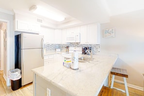 A modern kitchen with white cabinets, a marble countertop, a refrigerator, a microwave, and a sink. - Attractive and Convenient Gulf-Front Home Right on Beach with Shared Pool, Hot Tub (Gulf Shores)